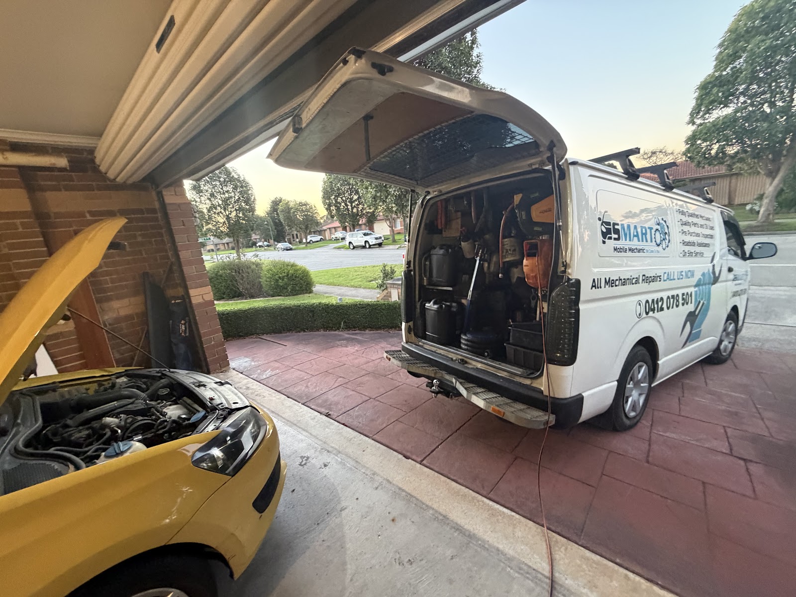 The Smart Mobile Mechanic van backed into a customer's driveway with a yellow car's bonnet up
