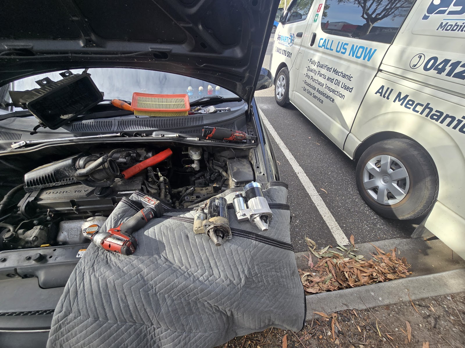 Engine bay repair on a moving blanket with the van parked alongside