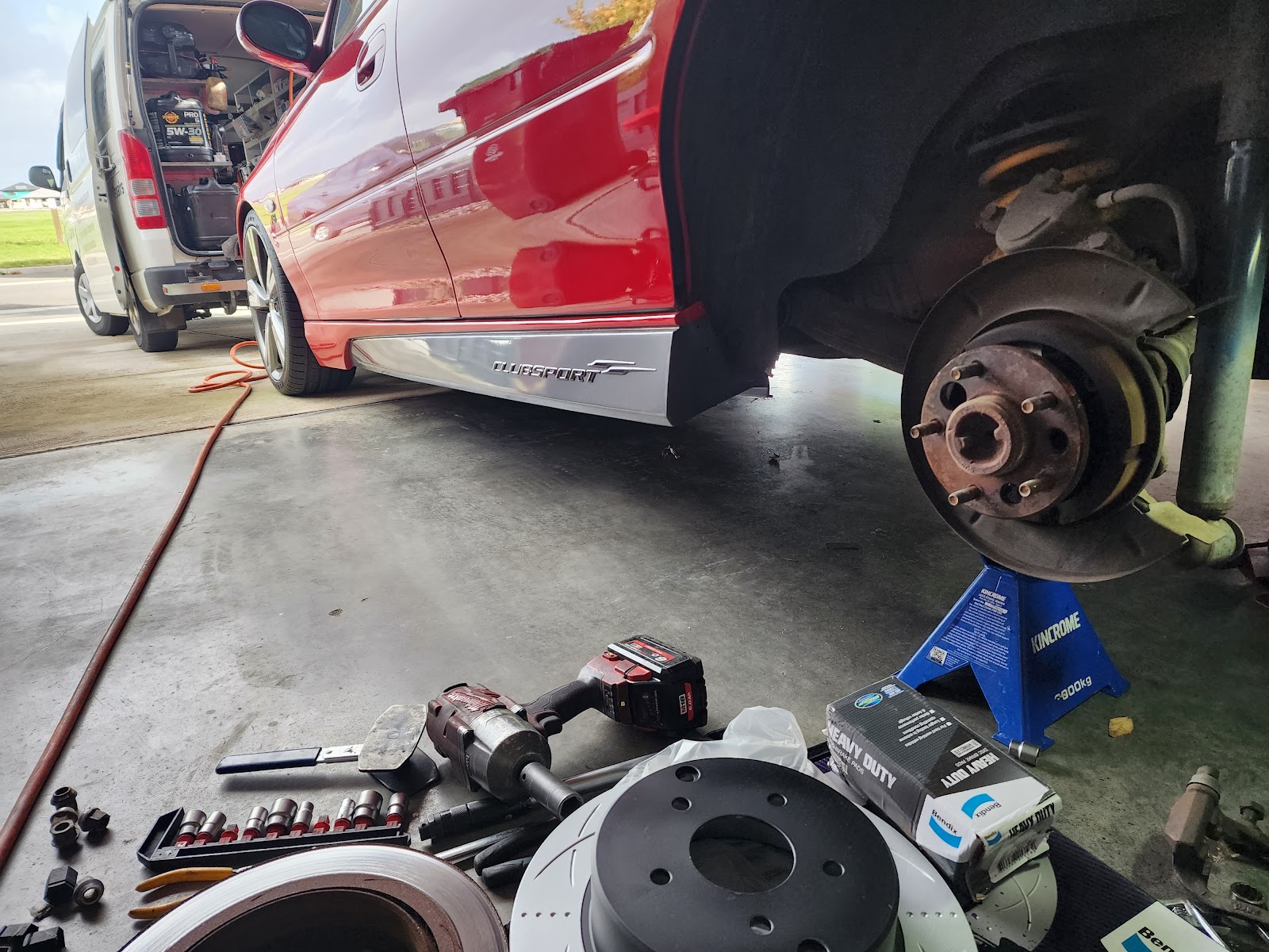 A red Commodore on stands with new brake rotors and pads ready to fit